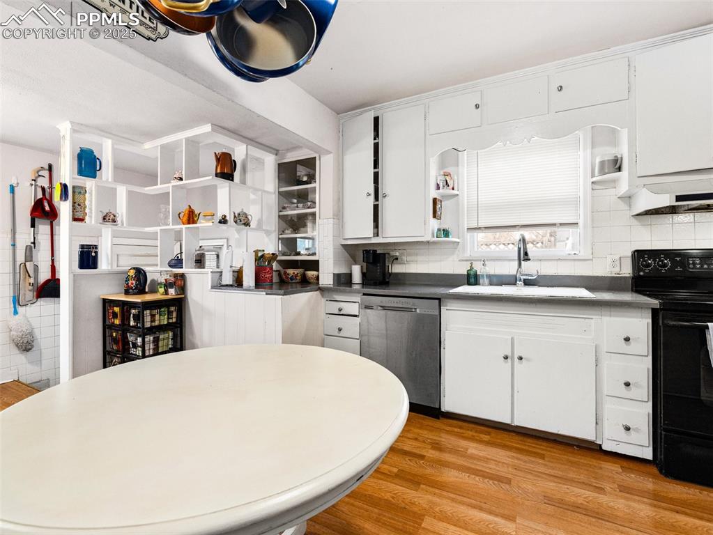 Kitchen with open shelves, white cabinets, light wood-style floors, and black range with electric stovetop