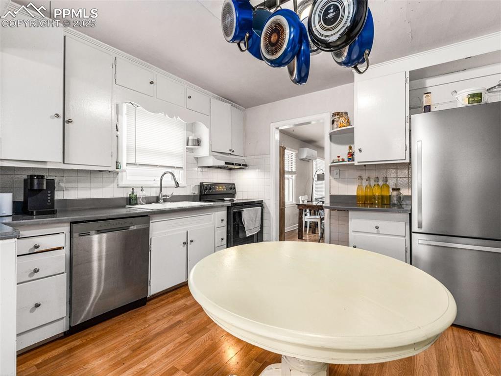 Kitchen featuring dark countertops, appliances with stainless steel finishes, white cabinetry, open shelves, and light wood-type flooring