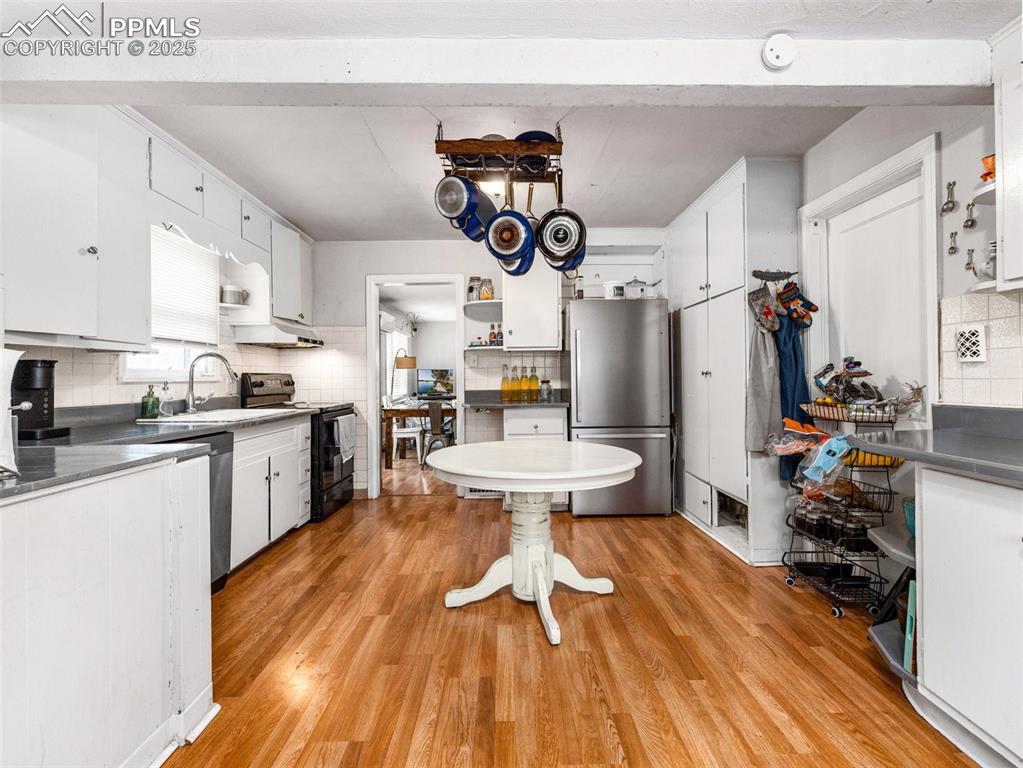 Kitchen featuring white cabinetry, dark countertops, freestanding refrigerator, backsplash, and black / electric stove