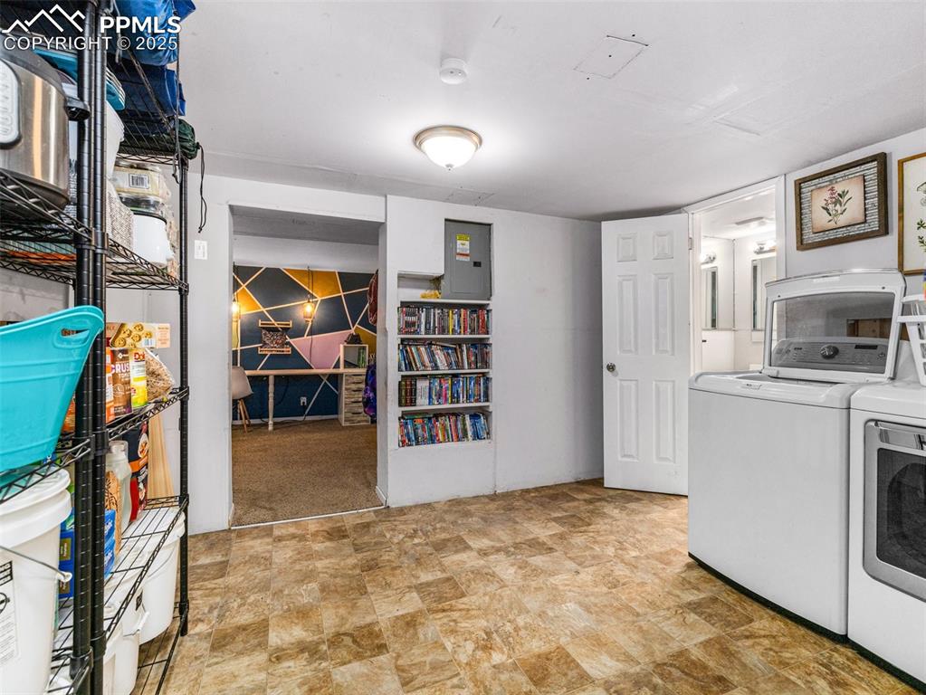 Laundry room featuring separate washer and dryer, electric panel, and stone finish flooring