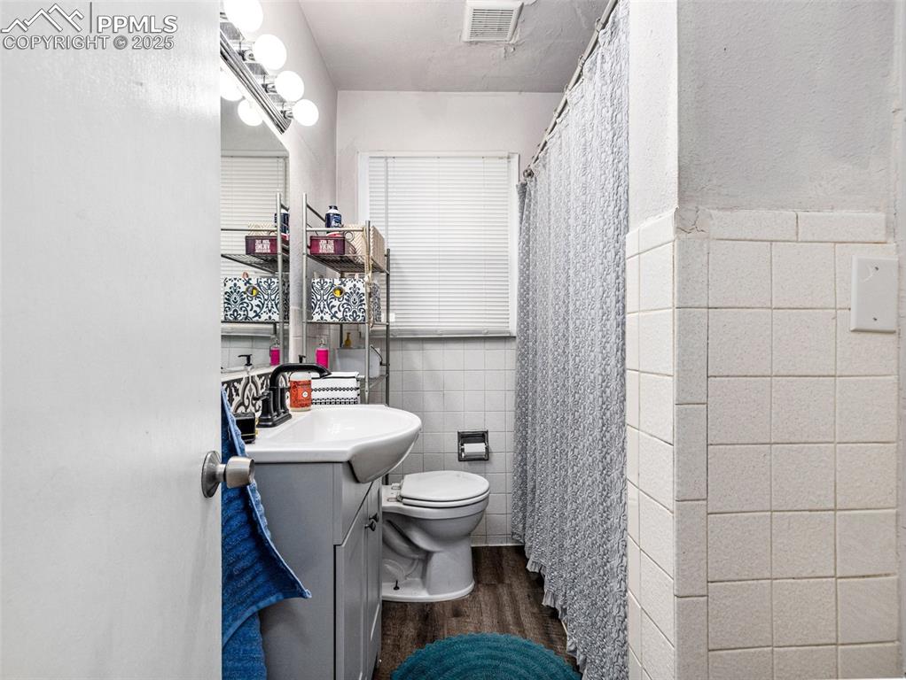 Full bath with tile walls, vanity, a shower with curtain, dark wood-type flooring, and wainscoting