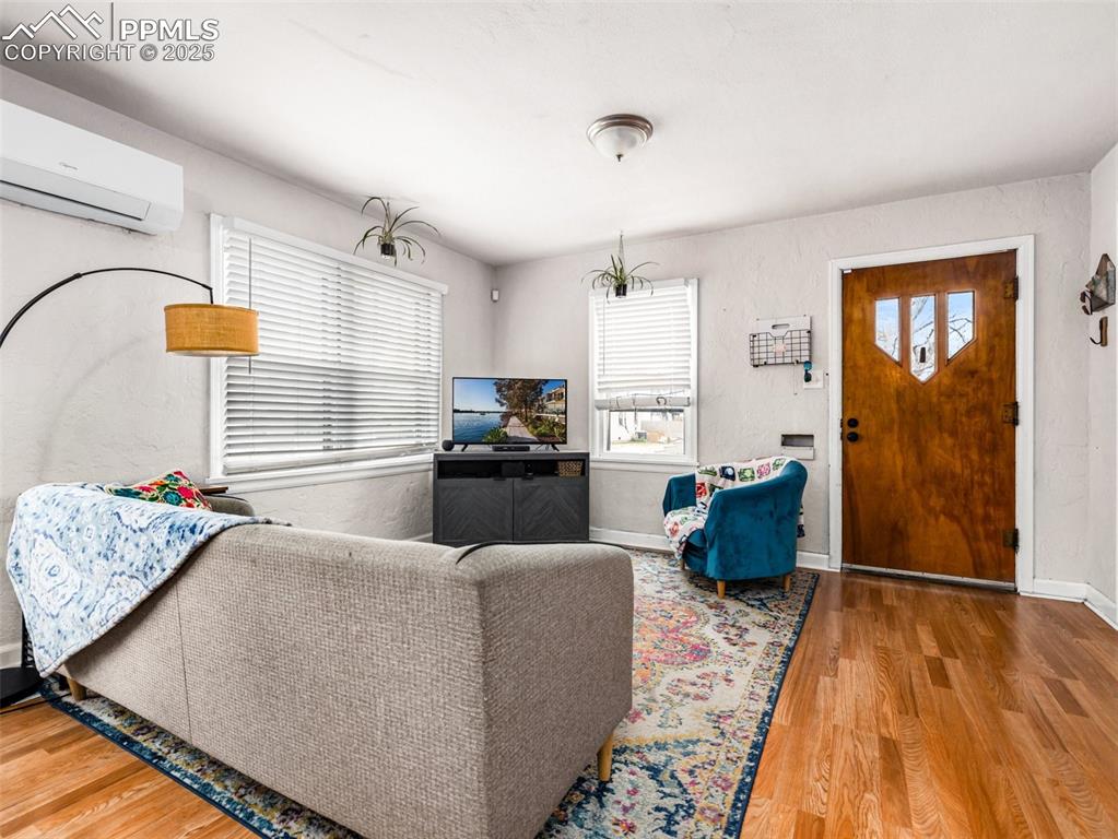 Living room with light wood finished floors, plenty of natural light, and a wall unit AC
