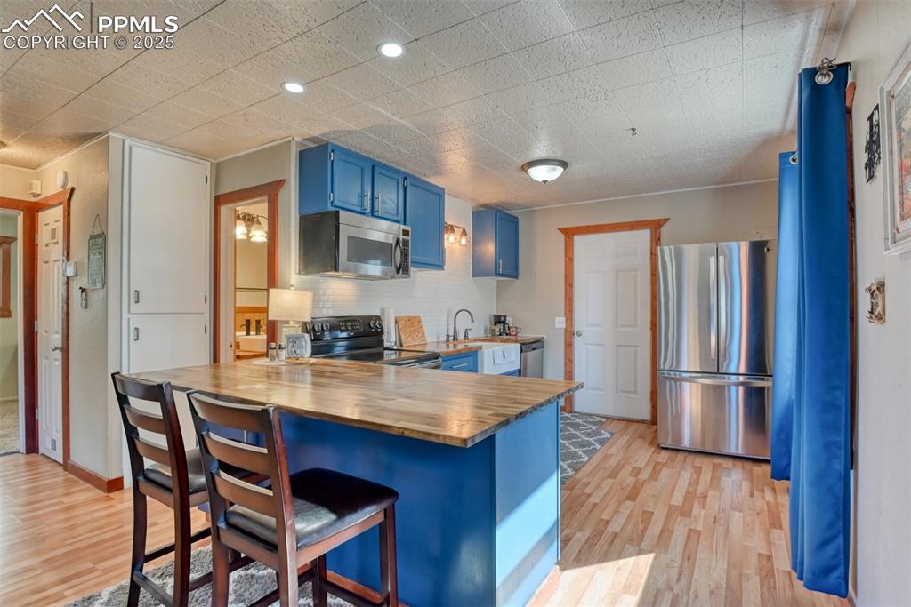 Kitchen with blue cabinets, butcher block countertops, a peninsula, appliances with stainless steel finishes, and a kitchen breakfast bar