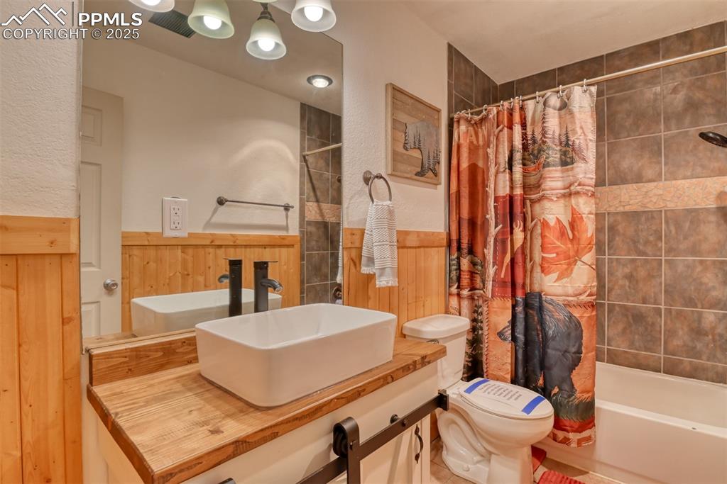 Full bath featuring shower / bathtub combination with curtain, vanity, and a wainscoted wall