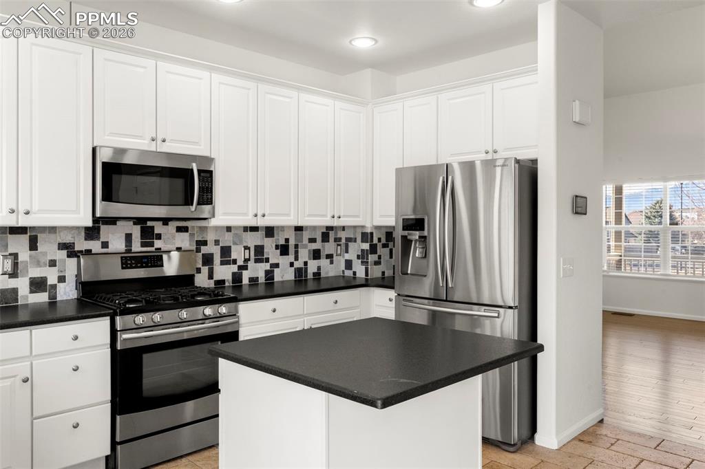 Kitchen with stainless steel appliances, tasteful backsplash, white cabinetry, a kitchen island, and recessed lighting