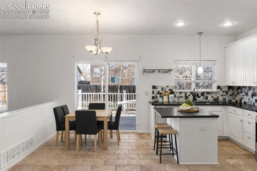 Kitchen with white cabinetry, a breakfast bar area, stone tile flooring, and dark solid countertops. virtually staged