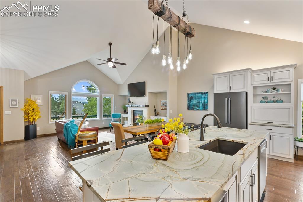 Kitchen with high vaulted ceiling, open floor plan, open shelves, light stone counters, and dark wood-style flooring