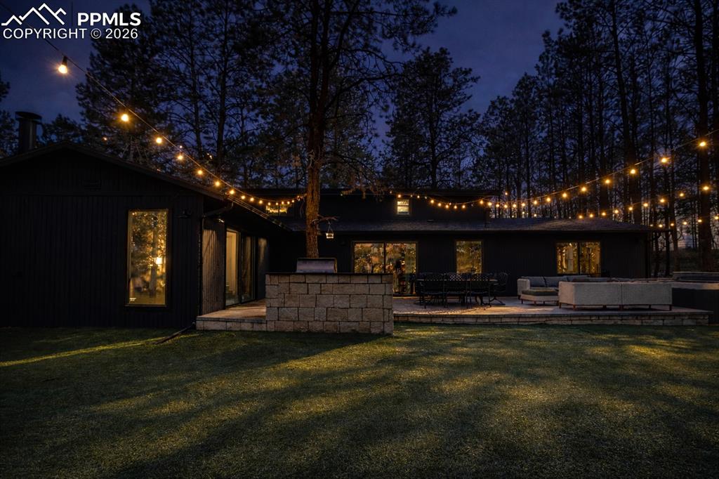 Back of house at twilight with a patio, an outdoor kitchen with living area, and a new turf lawn and new party lights