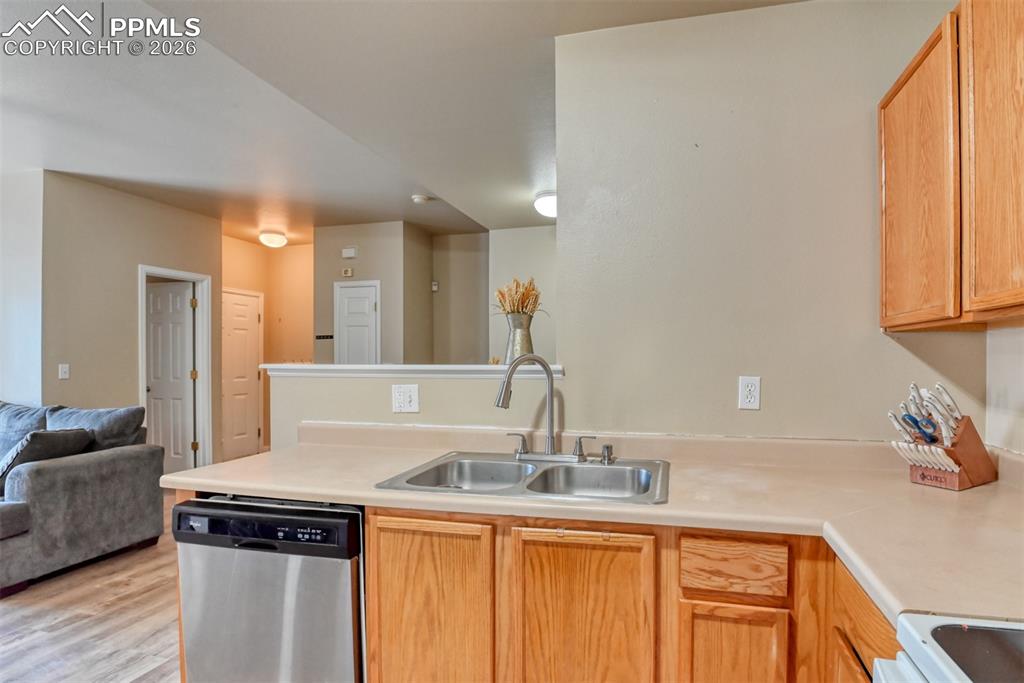 Kitchen with a peninsula, open floor plan, stainless steel dishwasher, light countertops, and white range oven