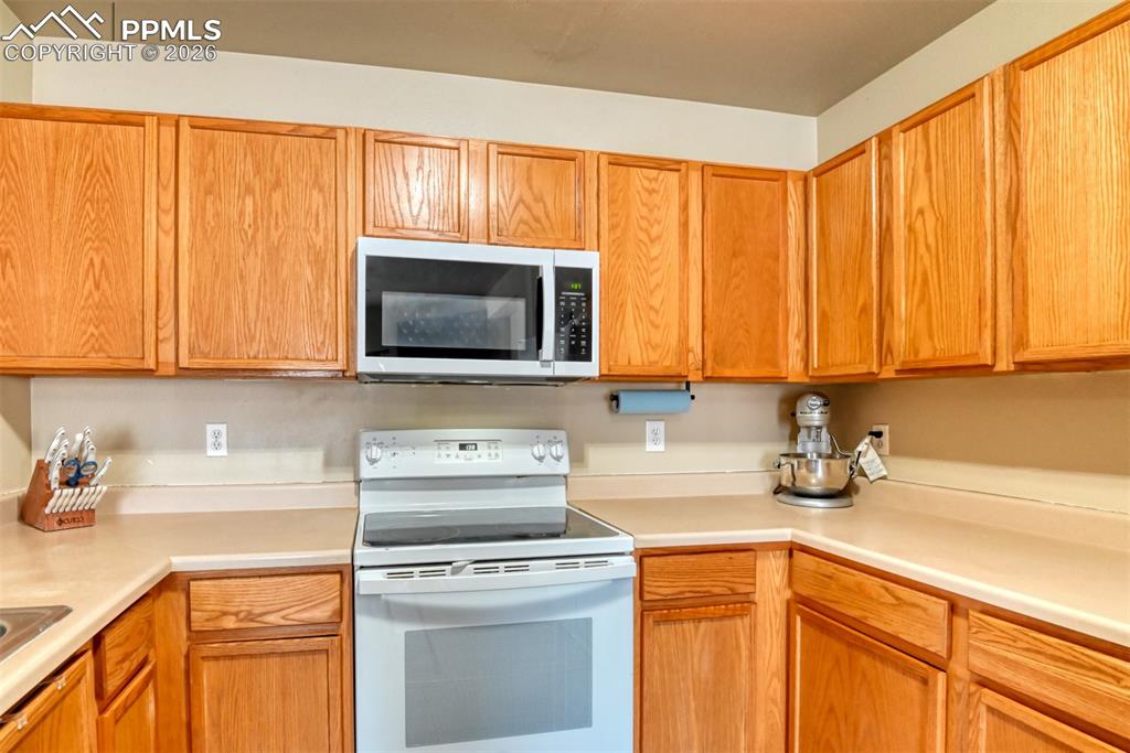 Kitchen with white electric stove, light countertops, and wood finish cabinetry