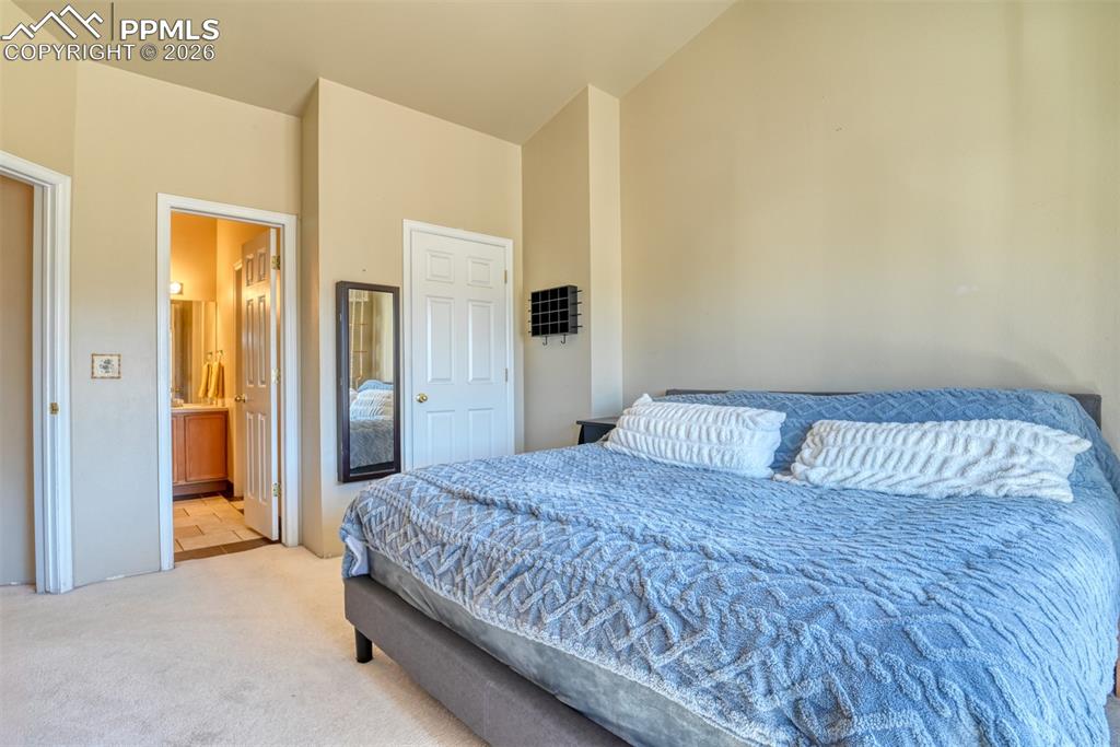 Bedroom with light carpet, ensuite bath, and lofted ceiling