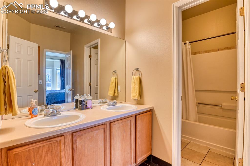 Bathroom featuring double vanity, connected bathroom, dark tile patterned flooring, and shower / bath combo