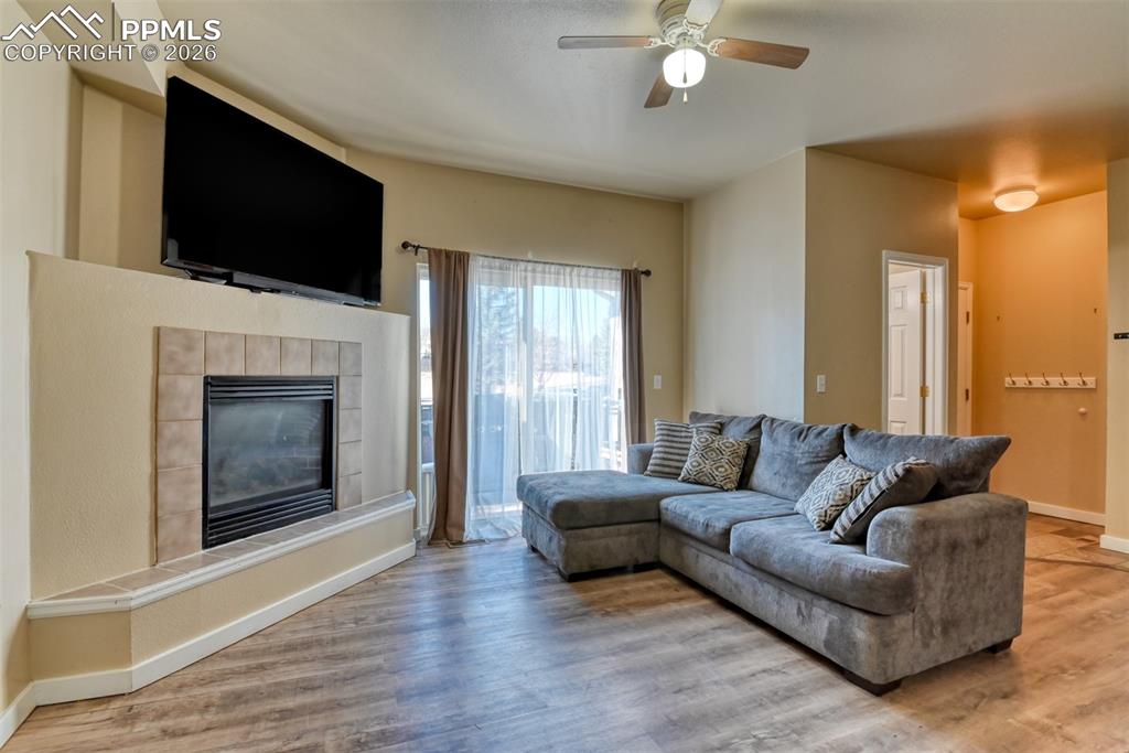 Living area with light wood-style floors, ceiling fan, and a tile fireplace