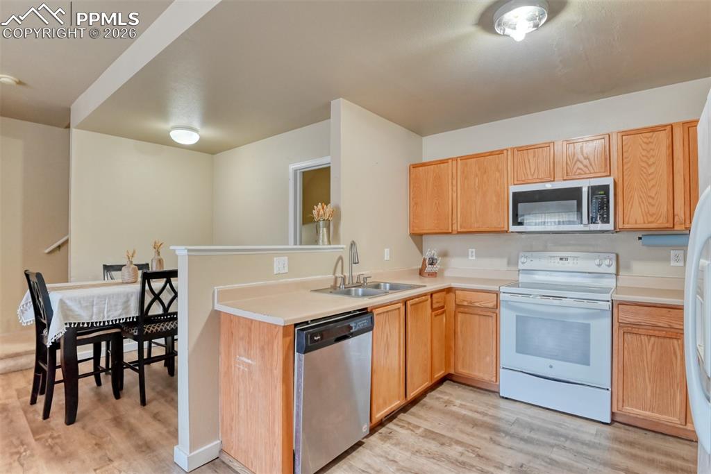 Kitchen featuring stainless steel appliances, light countertops, light wood-style flooring, and a peninsula