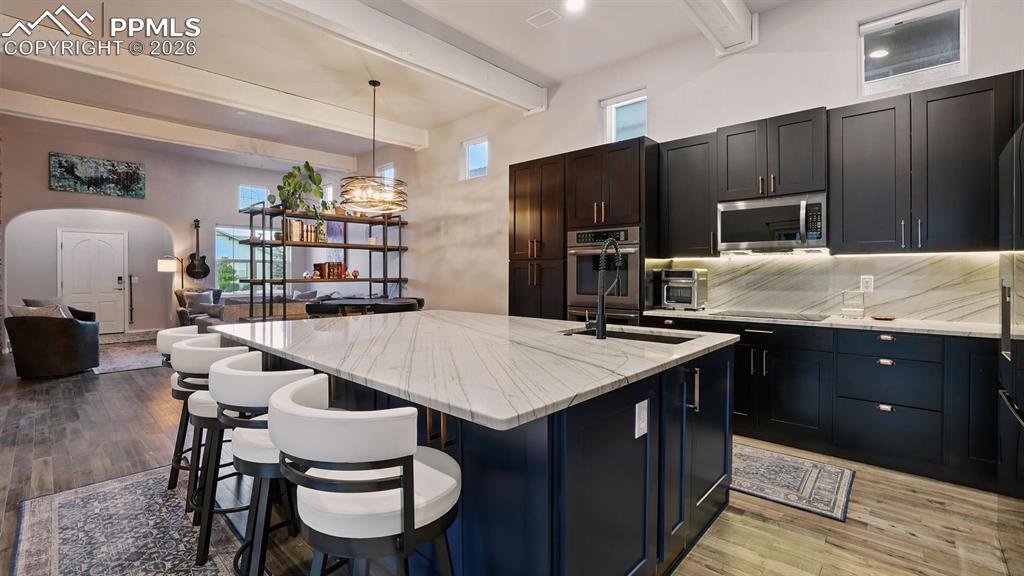 Chef inspired Kitchen  complete with a large island, breakfast bar, pantry, espresso cabinetry, quartz countertops, under-cabinet lighting, & stainless steel appliances.