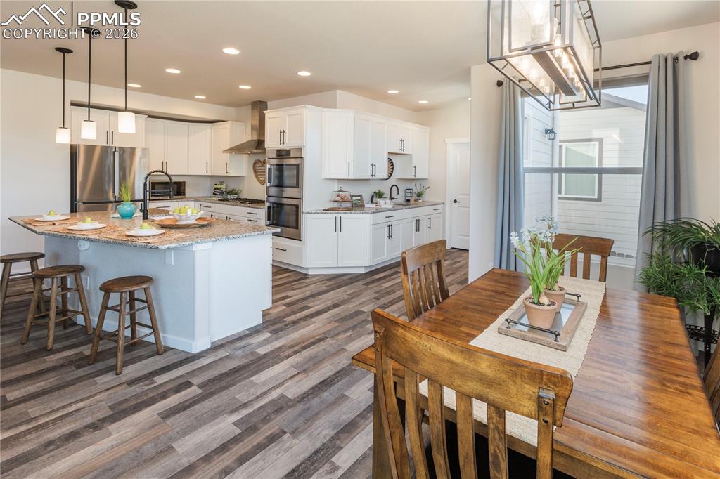 Kitchen with granite countertops, stainless steel appliances, white cabinetry, and LVP flooring.
