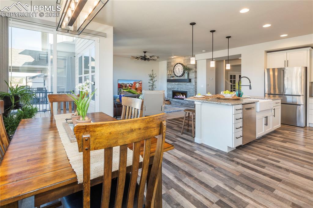 Kitchen with stainless steel appliances, light stone countertops, a stone fireplace, a kitchen island with sink, and pendant lighting