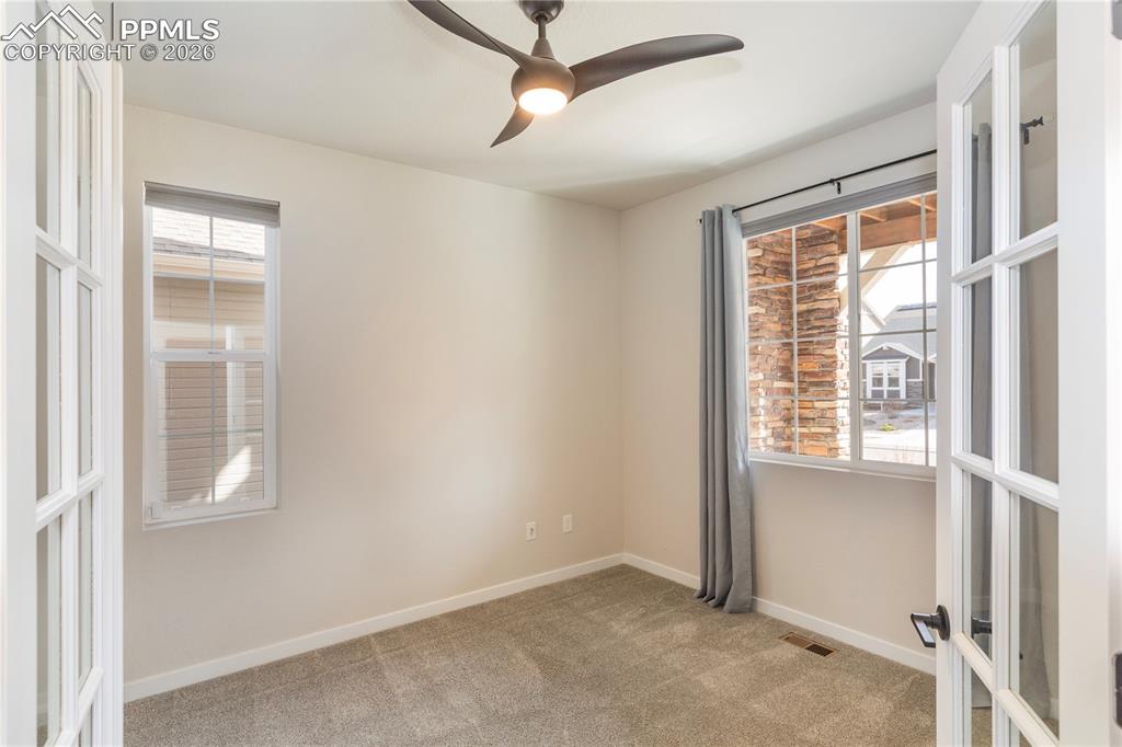 The office looks out onto the front porch and features a ceiling fan and french doors.