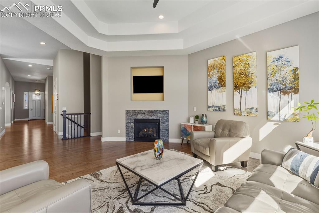 Living room with recessed lighting, wood finished floors, a warm lit fireplace, and a tray ceiling