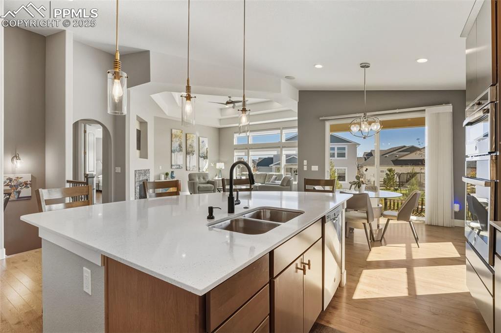 Kitchen featuring a ceiling fan, decorative light fixtures, light wood finished floors, light stone countertops, and a center island with sink
