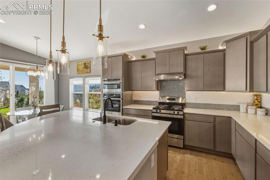 Kitchen with appliances with stainless steel finishes, decorative light fixtures, light wood-style flooring, recessed lighting, and light stone countertops
