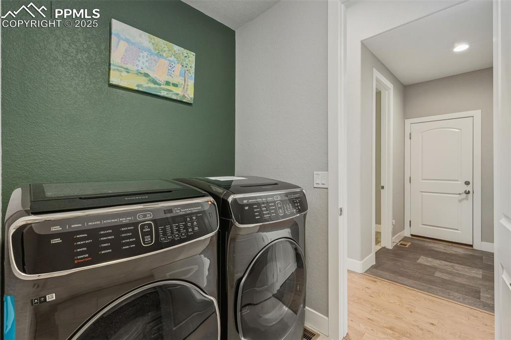 Laundry room with a textured wall, light wood finished floors, and washer and clothes dryer