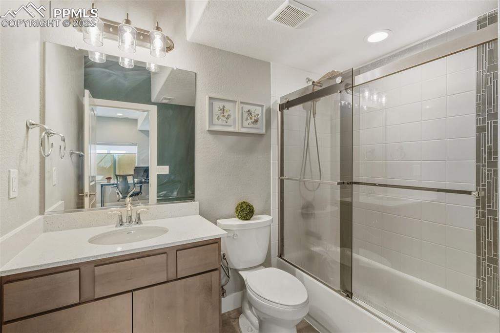 Full bath with a textured wall, bath / shower combo with glass door, vanity, and recessed lighting