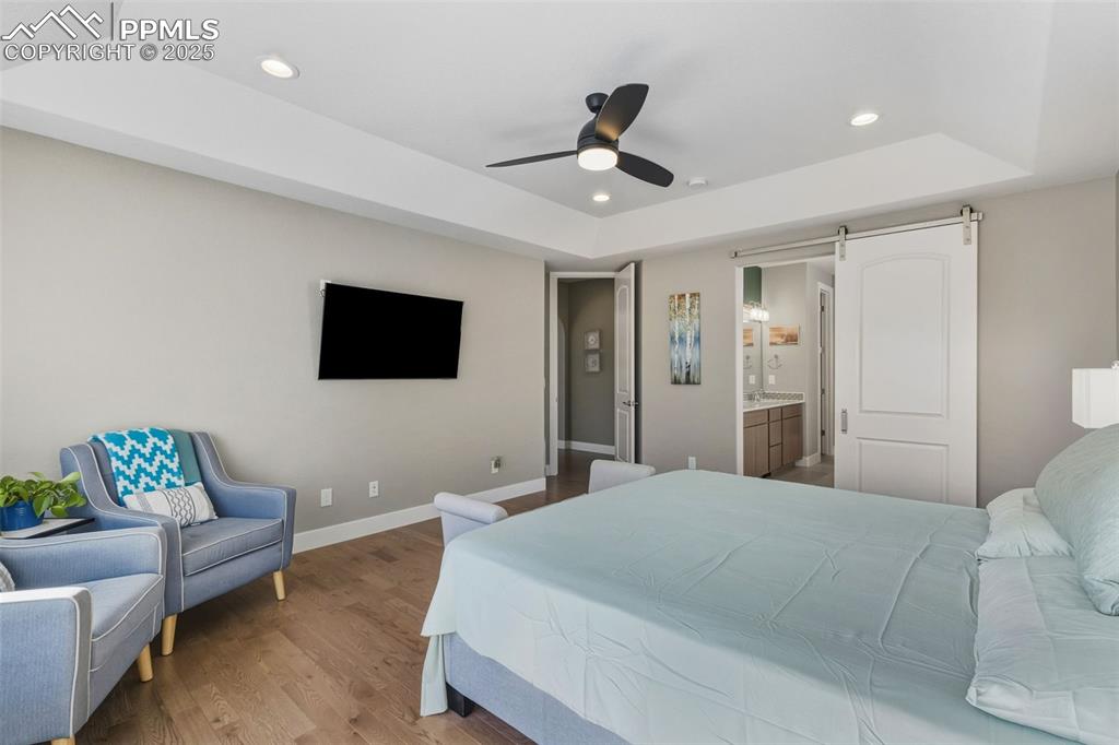 Bedroom featuring a barn door, wood finished floors, a raised ceiling, recessed lighting, and a ceiling fan