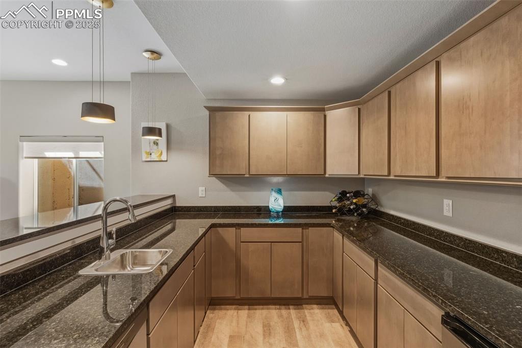 Kitchen featuring decorative light fixtures, light wood finished floors, dark stone countertops, recessed lighting, and brown cabinetry