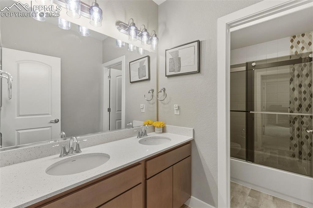 Bathroom featuring double vanity, enclosed tub / shower combo, a textured wall, and light wood-style floors