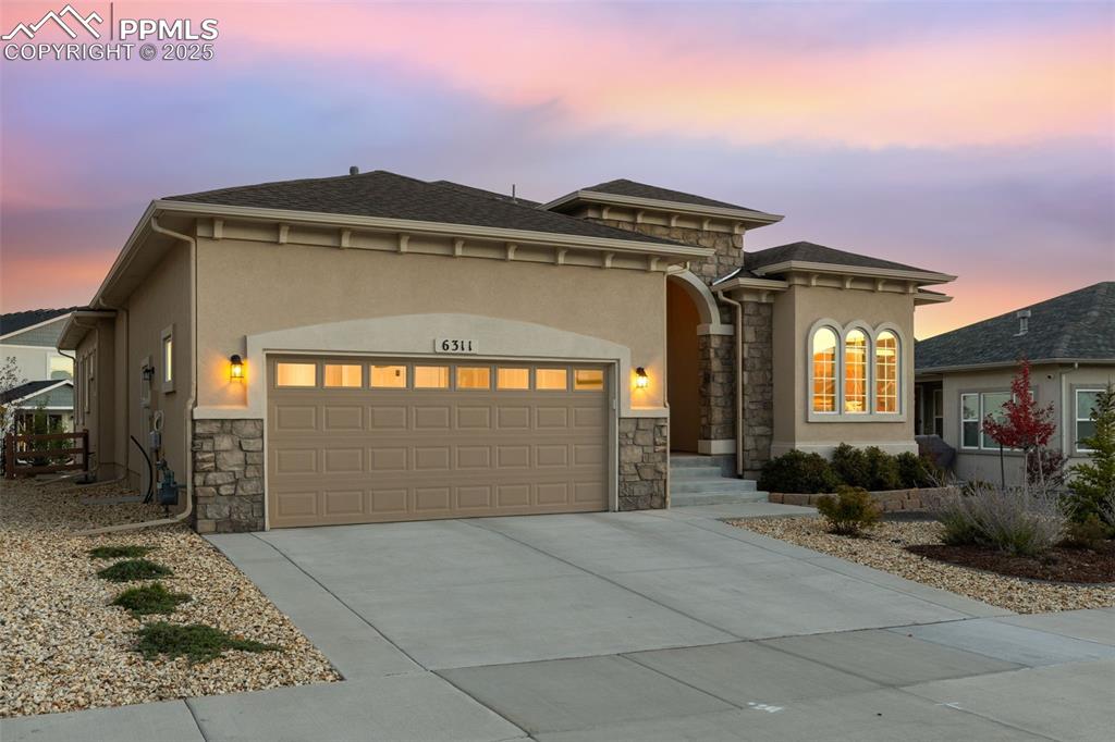 View of front of home with stone siding, an attached garage, and stucco siding
