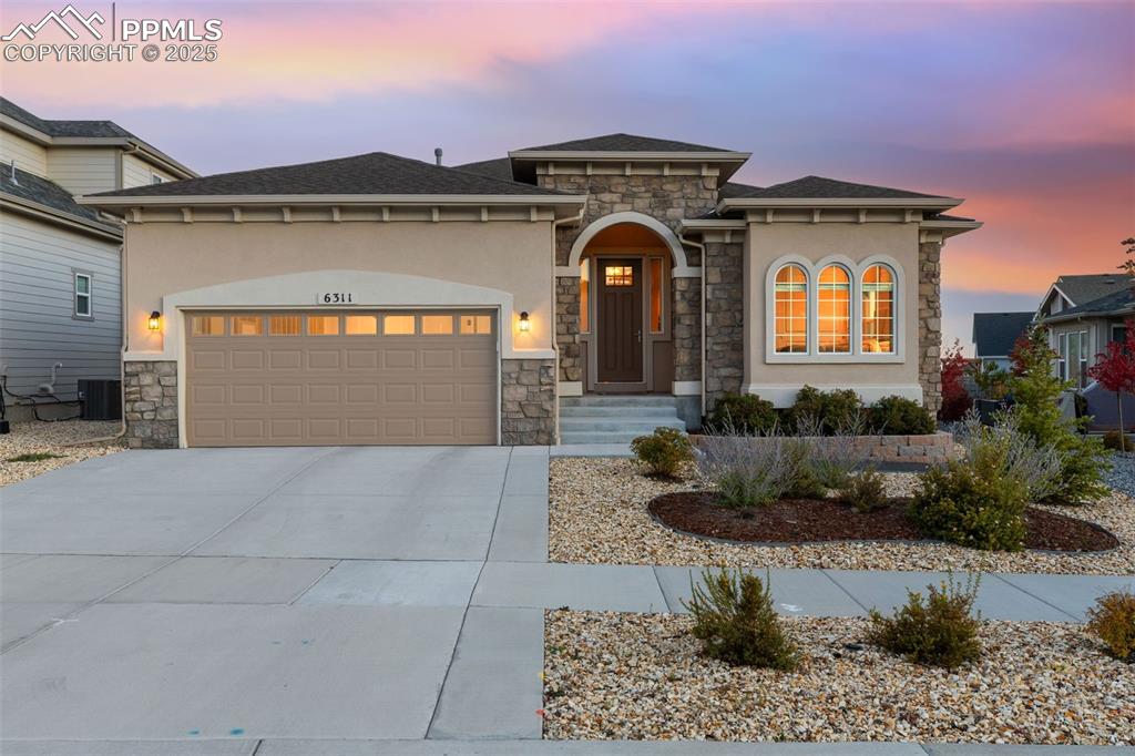 View of front facade featuring stone siding, driveway, an attached garage, and stucco siding