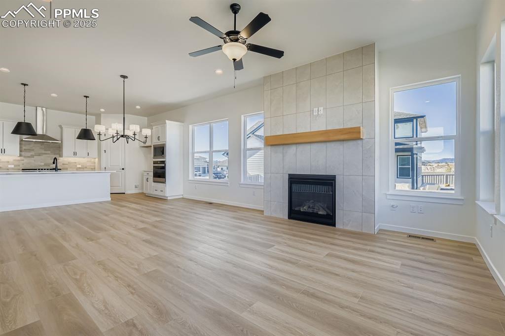 Unfurnished living room featuring light wood finished floors, a fireplace, a chandelier, recessed lighting, and a ceiling fan