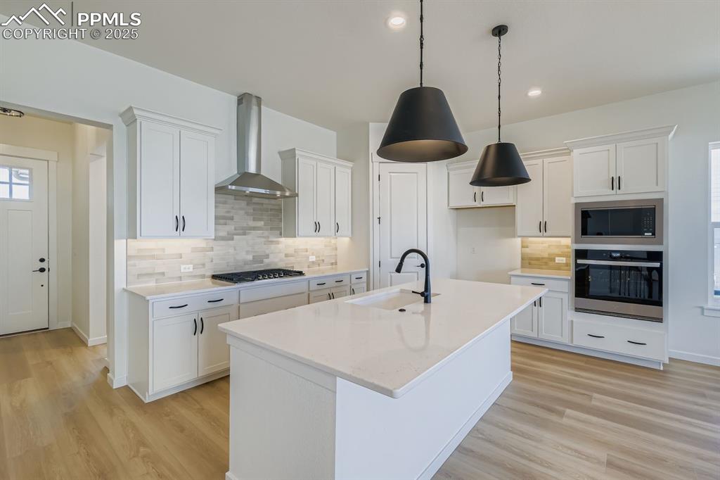 Kitchen featuring tasteful backsplash, stainless steel appliances, white cabinetry, light wood-style floors, and wall chimney exhaust hood