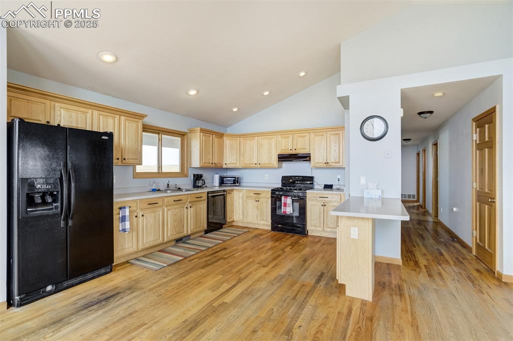 Kitchen with light brown cabinetry, black appliances, a peninsula, light wood-style floors, and light countertops