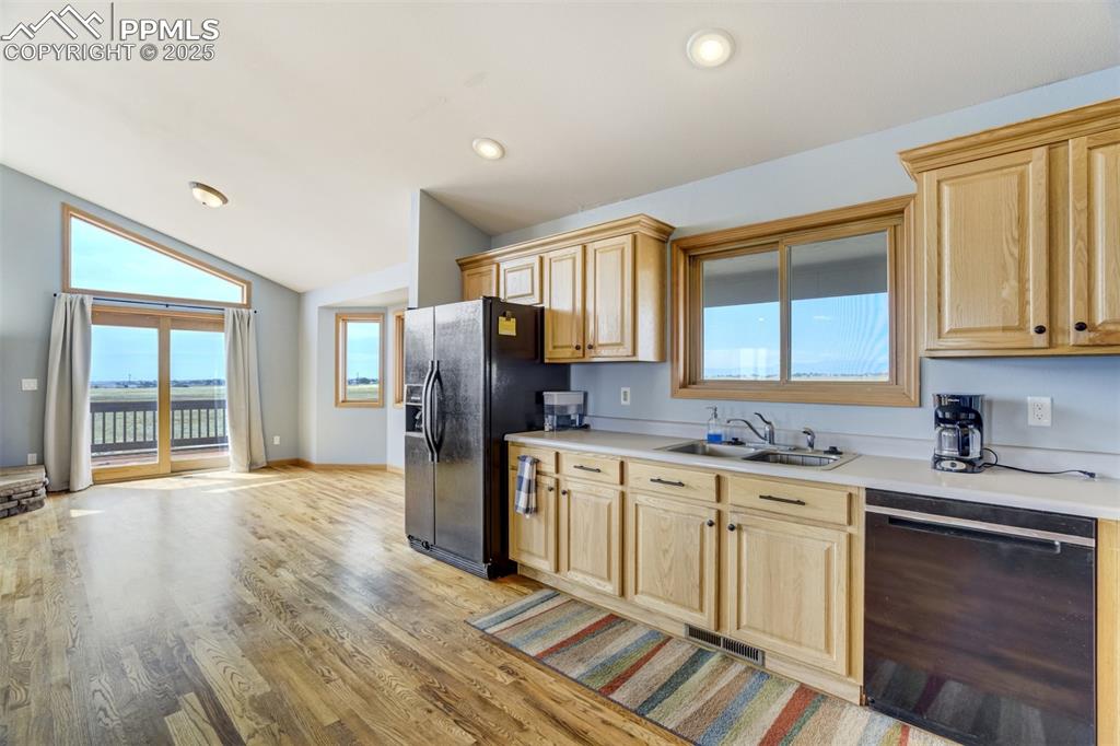 Kitchen with light brown cabinets, black appliances, vaulted ceiling, light wood finished floors, and light countertops