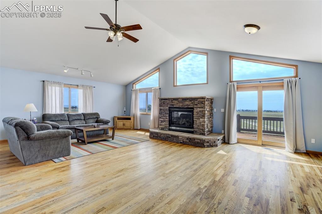 Living area with wood finished floors, a ceiling fan, a fireplace, and high vaulted ceiling