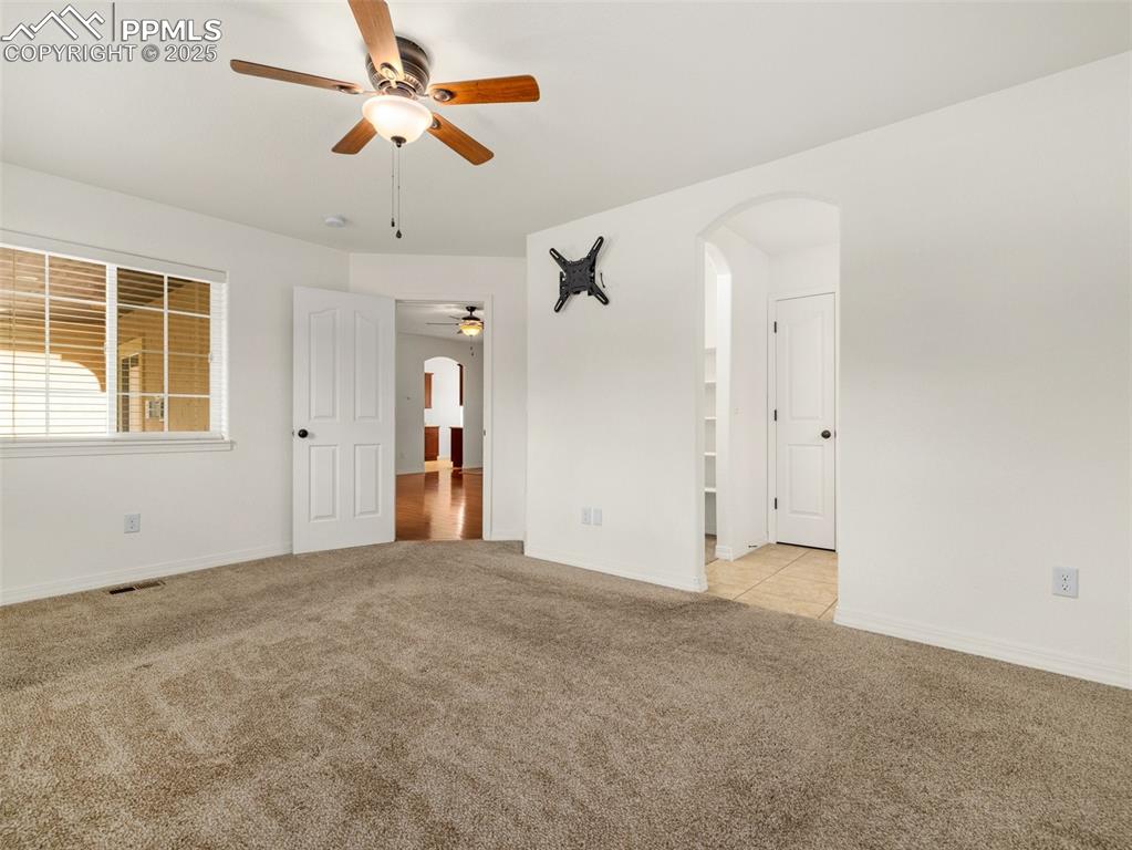 Primary bed room with a ceiling fan, arched walkways, and light colored carpet
