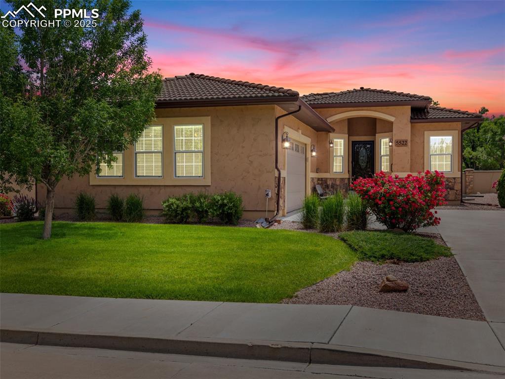 Mediterranean / spanish-style home with an attached garage, a front lawn, a tile roof, and stucco siding
