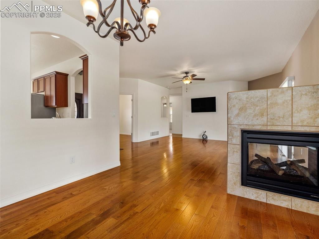 Unfurnished living room featuring a ceiling fan, a fireplace, light wood-type flooring, a chandelier, and arched walkways