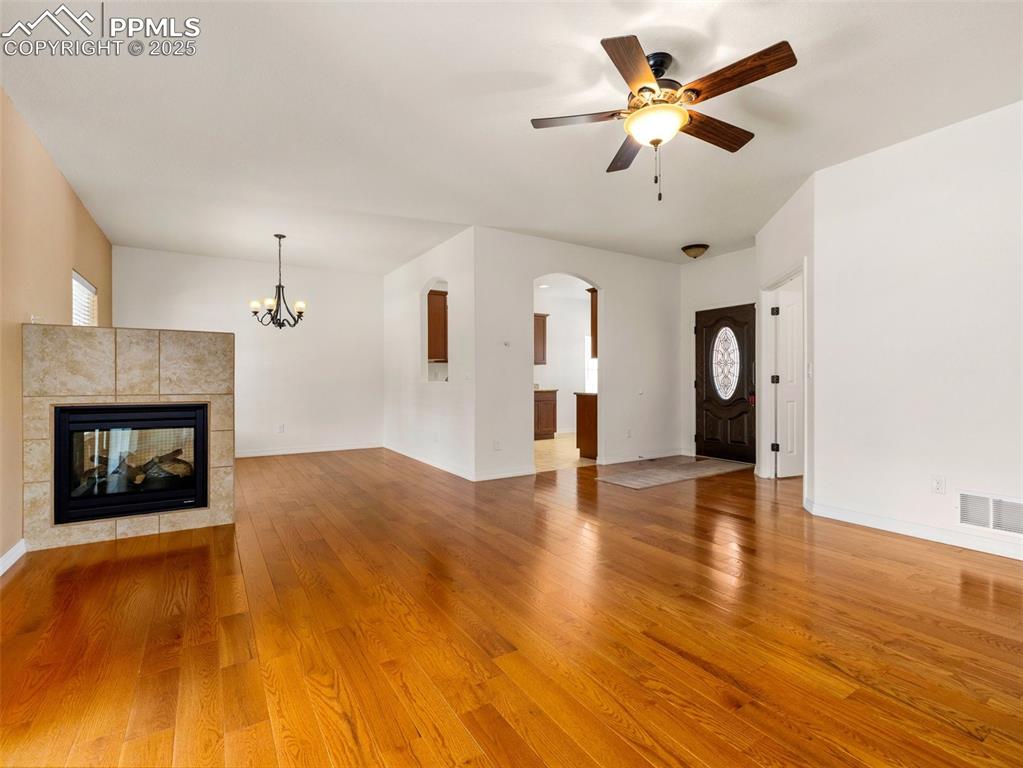 Unfurnished living room featuring wood finished floors, a tiled fireplace, arched walkways, a ceiling fan, and a chandelier