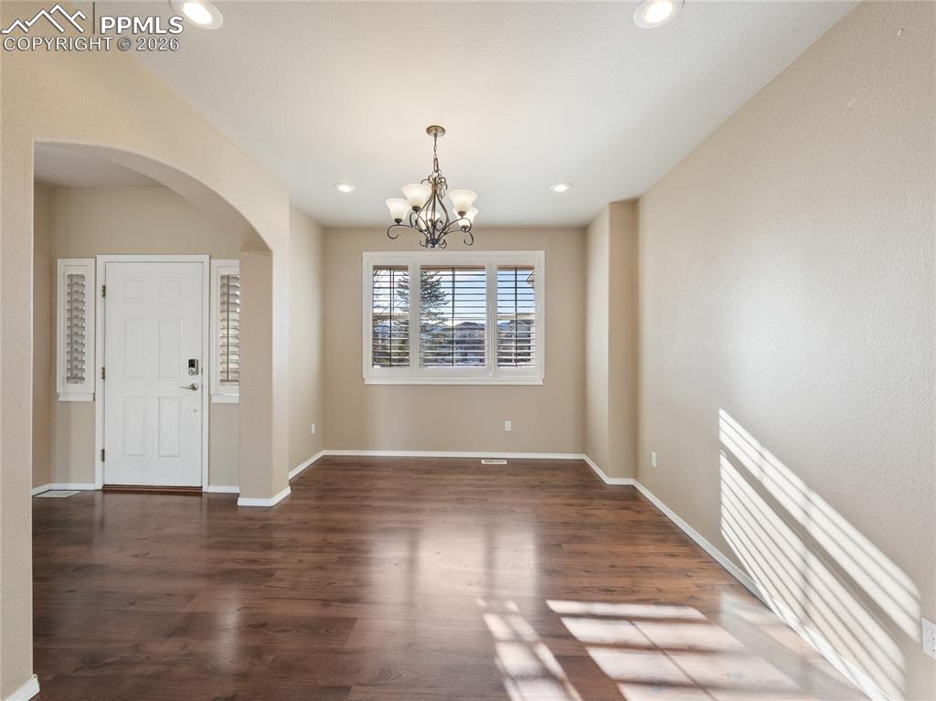 Unfurnished dining area featuring a chandelier, arched walkways, and dark wood-style floors