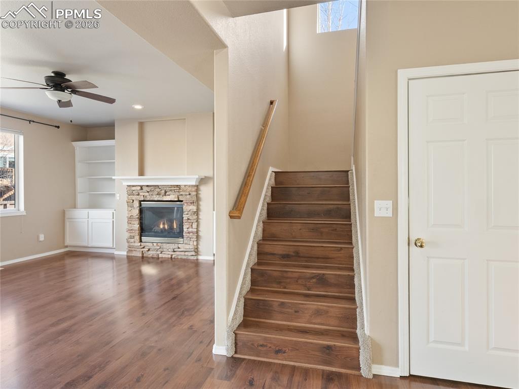 Stairs featuring a ceiling fan, wood finished floors, a stone fireplace, and recessed lighting