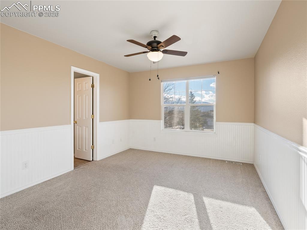 Carpeted upper level bedroom featuring ceiling fan and wainscoting