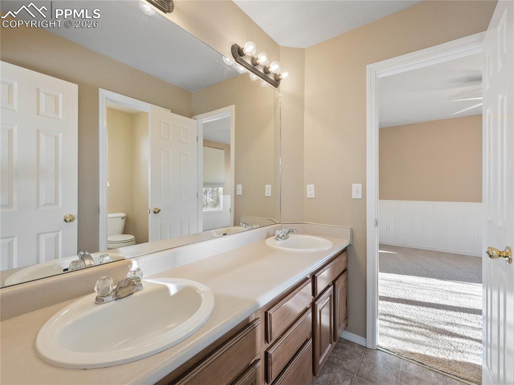 Jack and Jill bathroom with double vanity, light colored carpet, and wainscoting