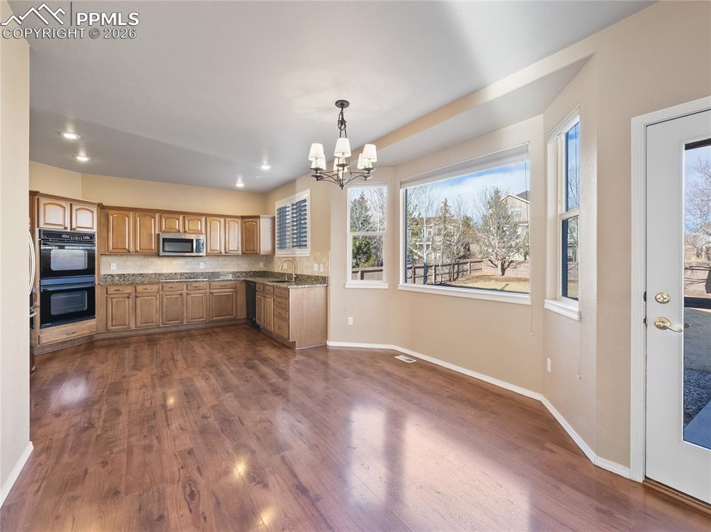 Kitchen featuring a chandelier, black appliances, dark wood-style floors, light stone counters, and wood finish cabinets