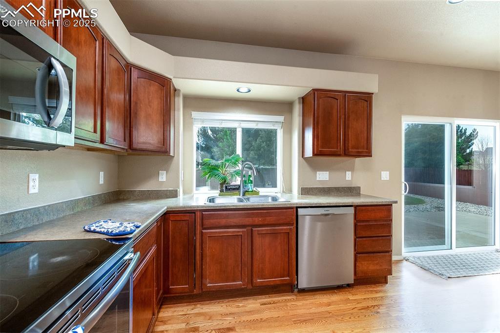 Kitchen featuring appliances with stainless steel finishes, light wood-style flooring, brown cabinets, recessed lighting, and light countertops