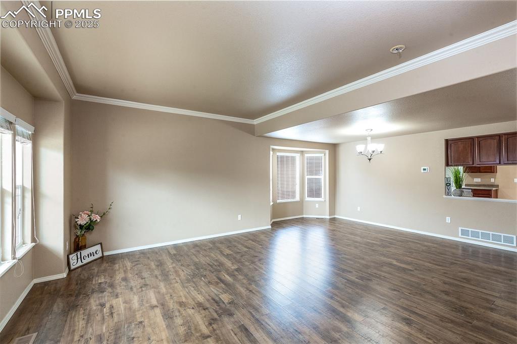Unfurnished room featuring a chandelier, dark wood-style floors, crown molding, and a pendent fire sprinkler