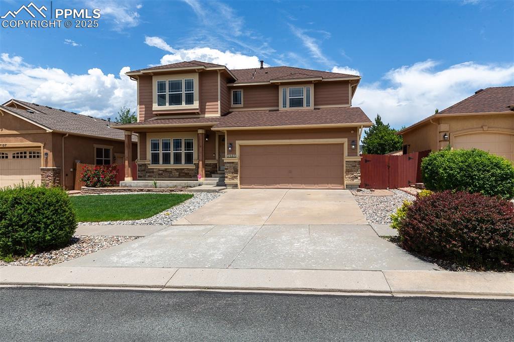 Prairie-style house featuring stone siding, driveway, a garage, and a gate