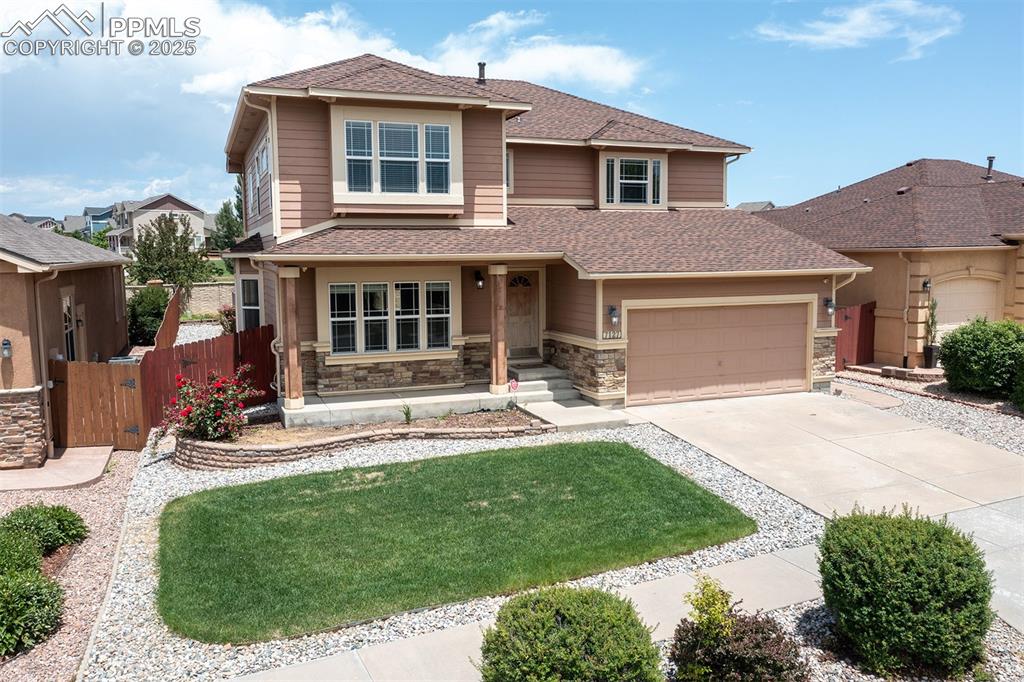 View of front of property featuring a garage, driveway, a shingled roof, and stone siding